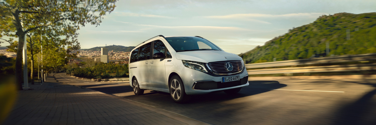 a white Mercedes-Benz Vito driving on a road surrounded by trees and greenery